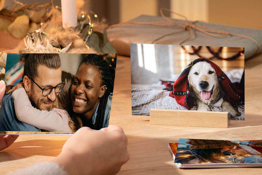 A hand holding a photo of a dog in a red scarf and another photo of two people hugging.