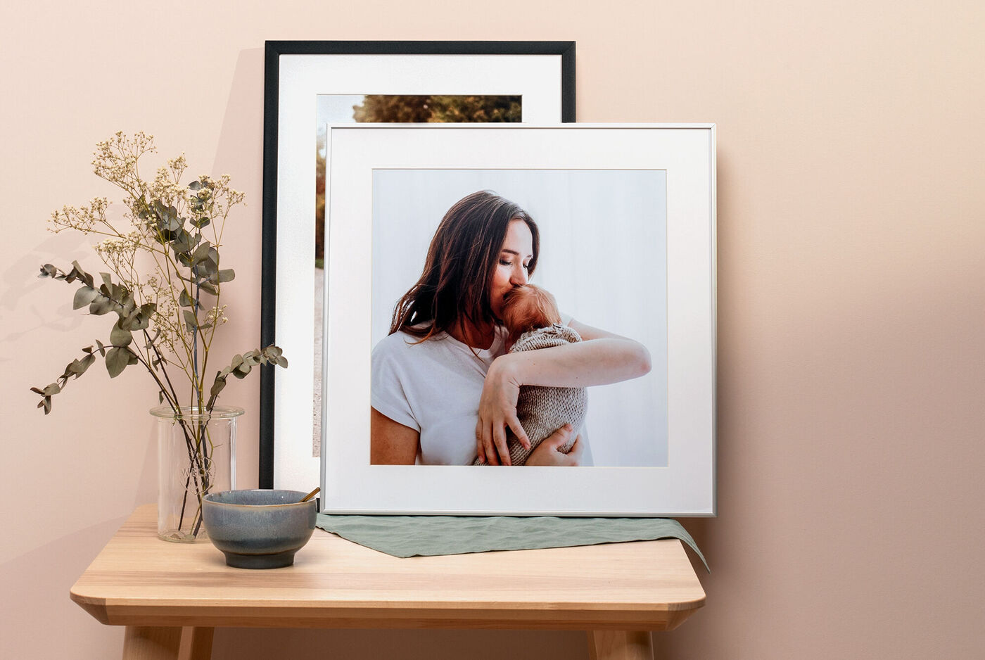Framed photo of a person with a pet on a wooden table, surrounded by a vase with flowers and a small dish.