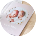 Two newborns, Lin and Tilda, lie in a gentle embrace on a soft background